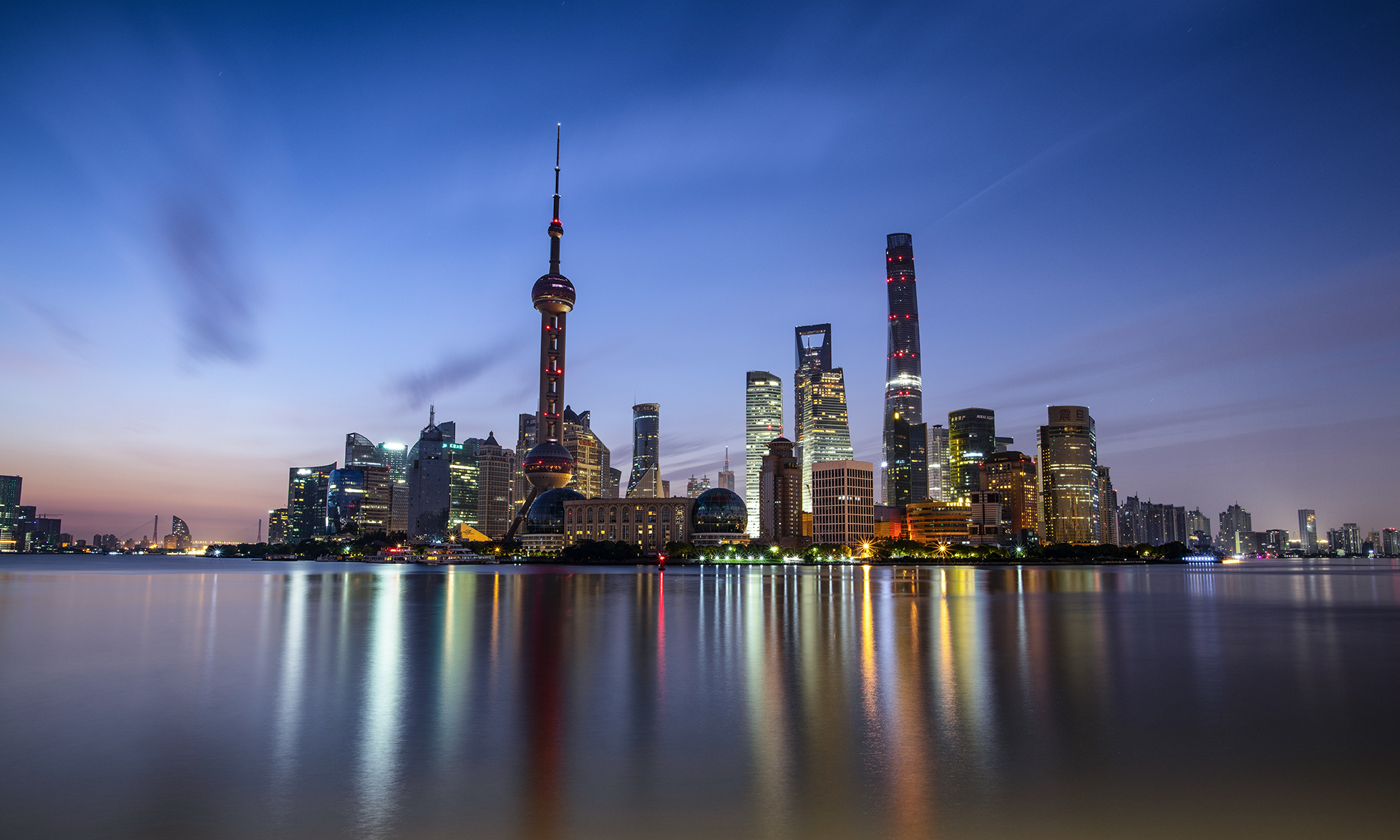 lights of Shanghai's Puxi downtown skyscrapers reflect over the water from the view of the Bund